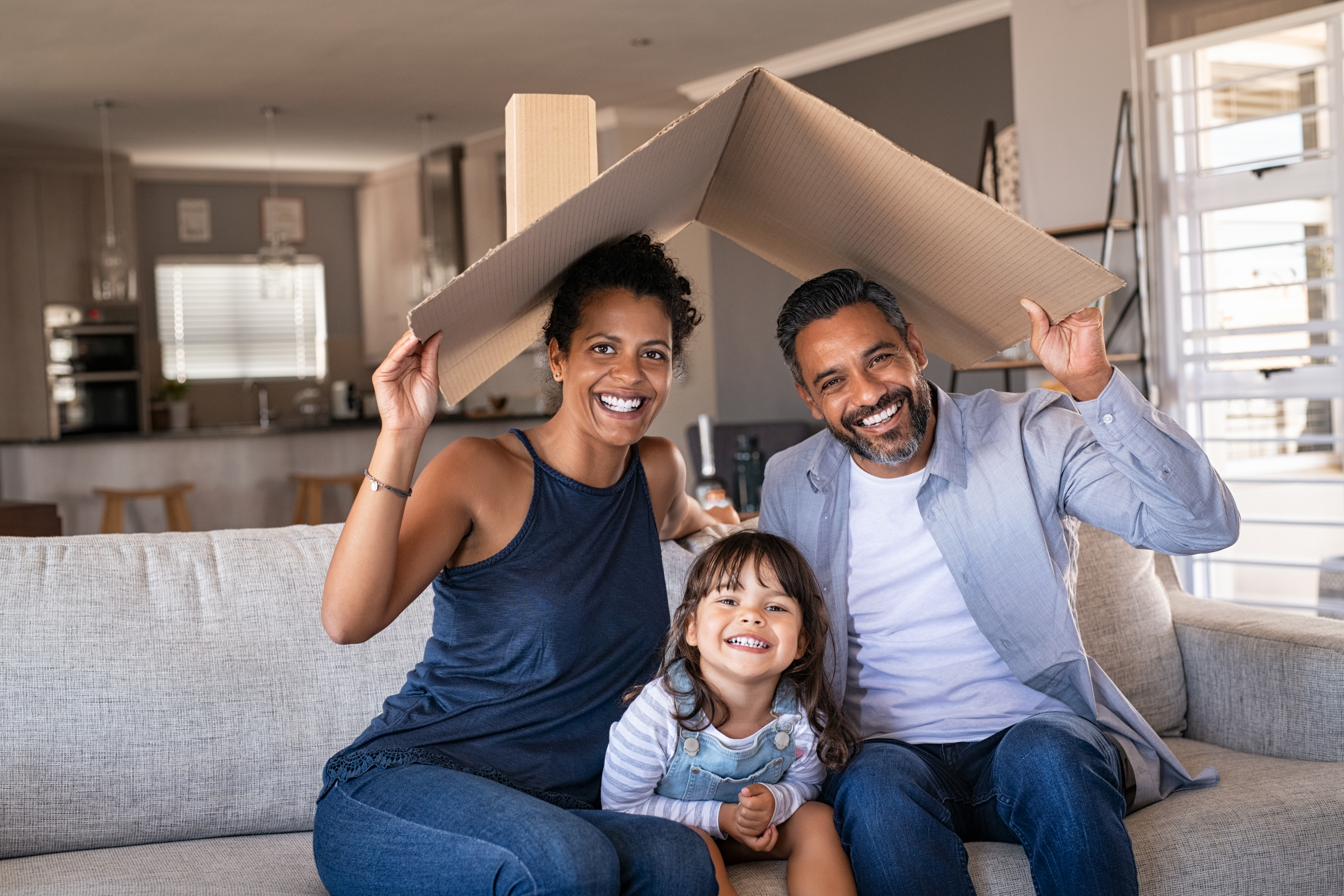 Family sitting on the couch holding a piece of cardboard over their head in the shape of a roof