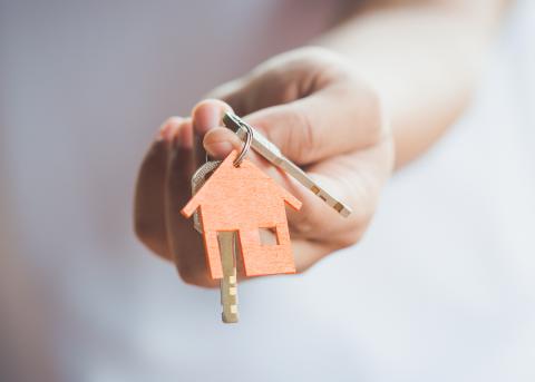 Person handing over keys with a house keychain